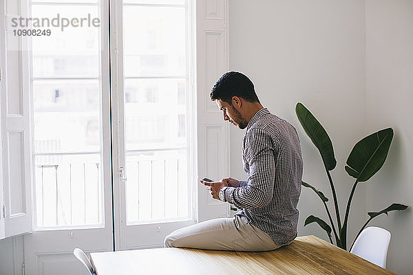 Young businessman sitting on desk using smart phone