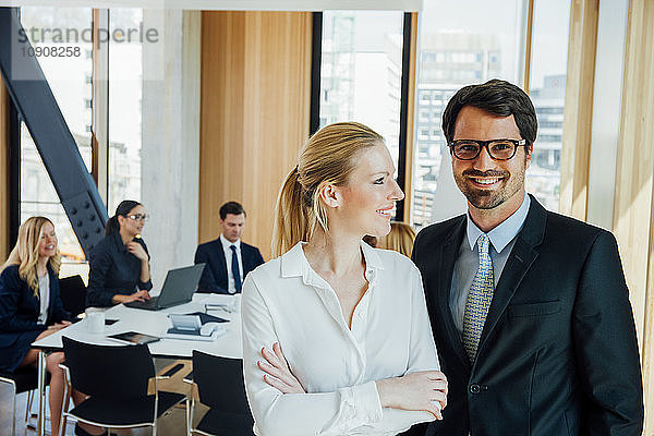 Businessman and businesswoman in office with meeting in background