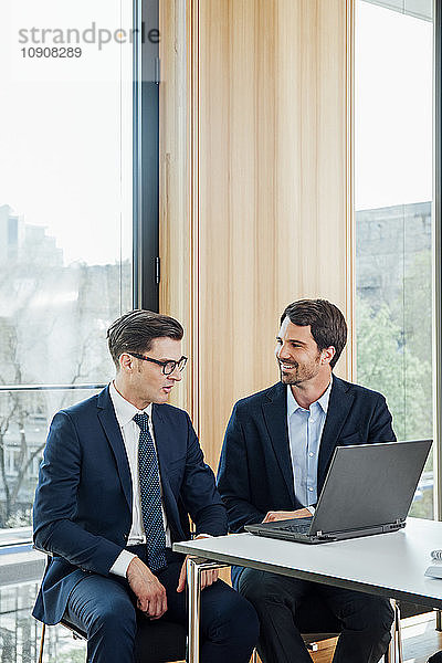Two businessmen with laptop talking in office