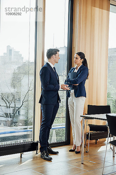 Businessman and businesswoman in office talking at the window
