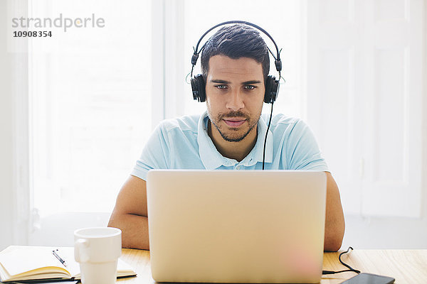 Junger Mann im Büro mit Kopfhörer und Laptop