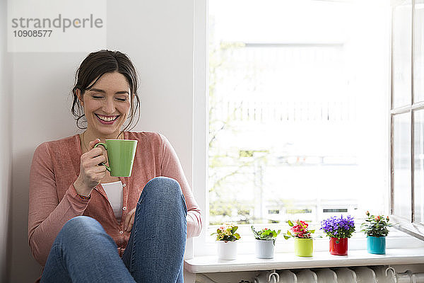 Happy young woman with cup of coffee sitting at the window