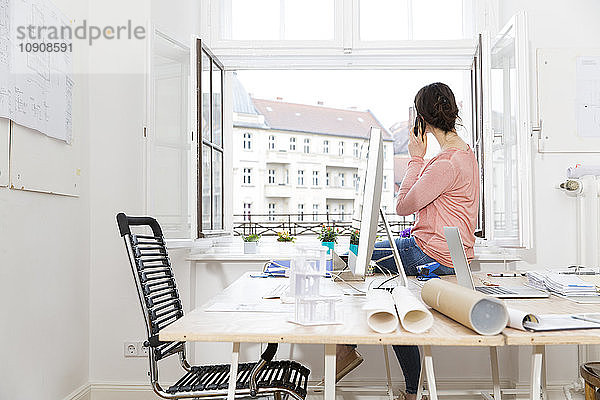 Woman in office sitting on table telephoning