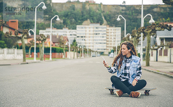 Junge Frau beim Musikhören auf dem Skateboard