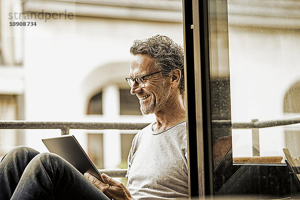 Lächelnder Mann auf dem Balkon sitzend mit digitalem Tablett