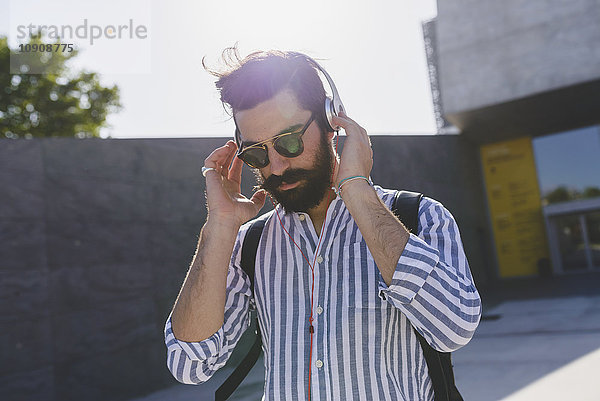 Bartiger junger Mann mit Sonnenbrille  Musik hören mit Kopfhörer