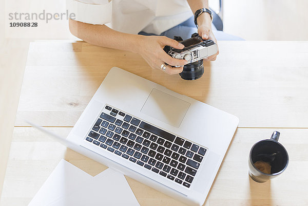 Frau am Schreibtisch sitzend mit Laptop und Kaffeetasse mit Digitalkamera  Teilansicht