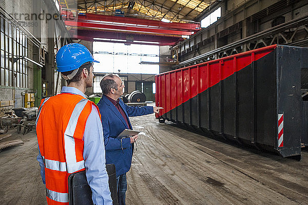 Manager and worker talking at container in factory hall