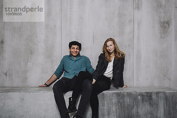 Young couple sitting in front of concrete wall  smiling