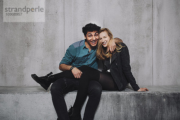 Young couple sitting in front of concrete wall  laughing