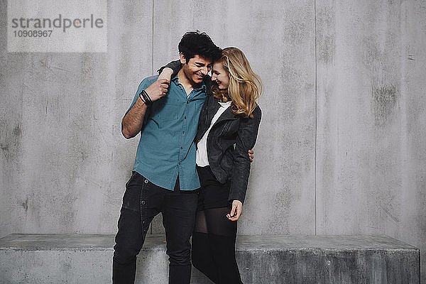 Young couple embracing in front of concrete wall