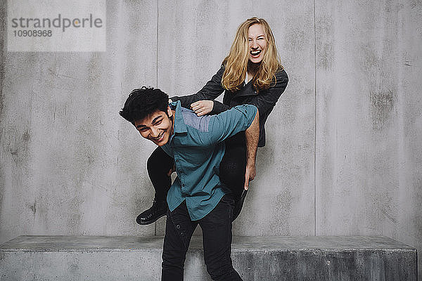 Young couple sitting in front of concrete wall  piggyback