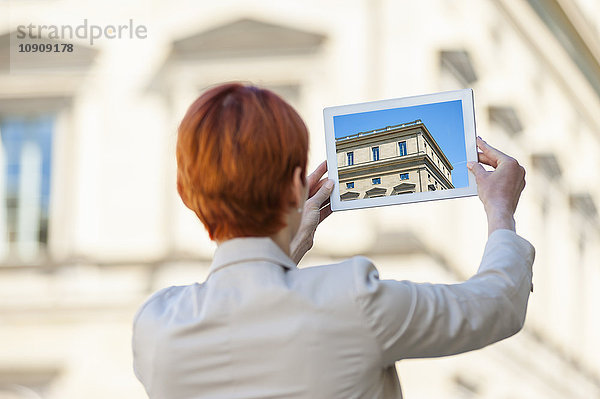 Junge Frau im Freien mit digitalem Tablett beim Fotografieren eines Hauses