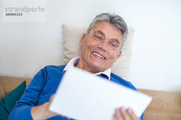 Lächelnder älterer Mann auf der Couch liegend mit digitalem Tablett