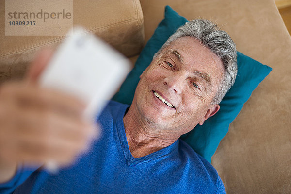 Lächelnder älterer Mann auf der Couch liegend mit Handy