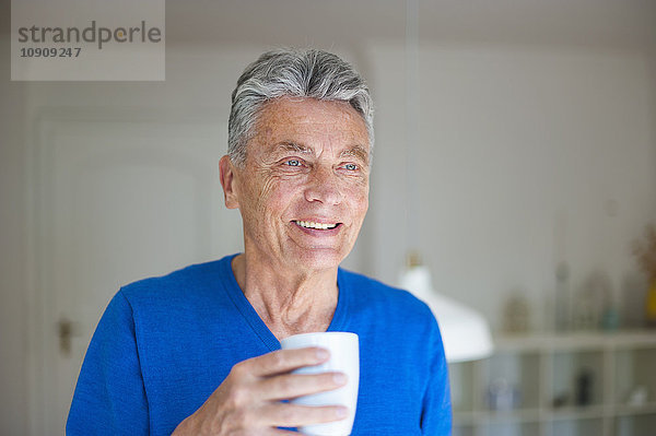 Lächelnder älterer Mann zu Hause mit einer Tasse Kaffee