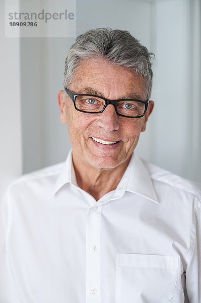 Porträt eines lächelnden älteren Mannes mit Brille und weißem Hemd