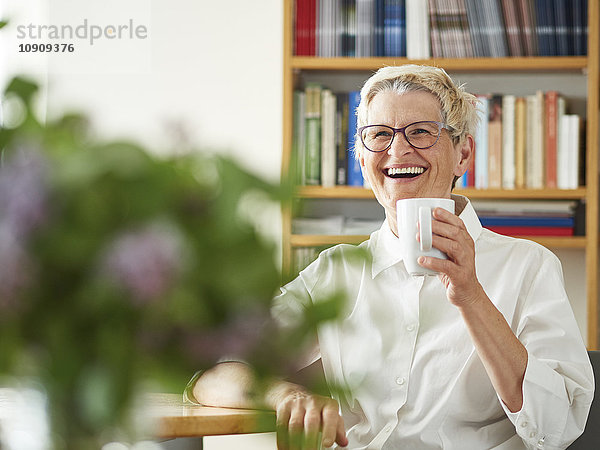 Porträt der lachenden Seniorin mit Tasse Kaffee zu Hause