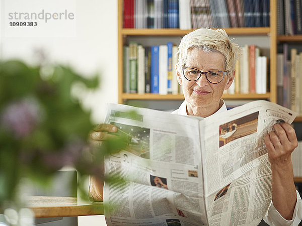 Porträt einer älteren Frau beim Zeitungslesen zu Hause