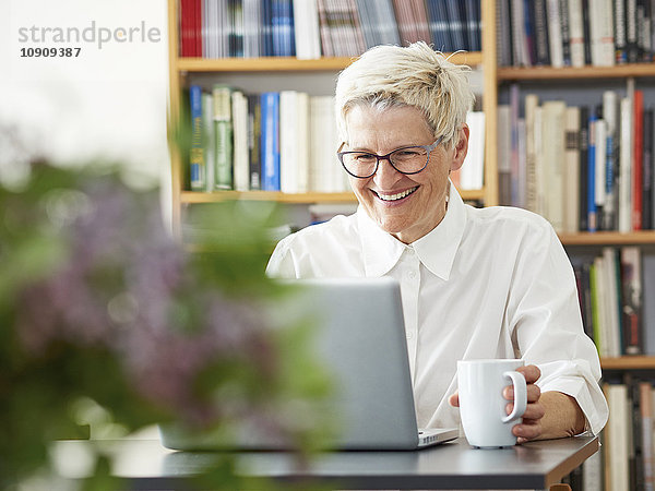 Porträt der lachenden Seniorin mit dem digitalen Tablett zu Hause