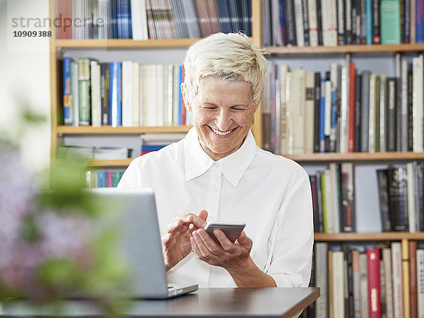 Porträt der lächelnden Seniorin mit digitalem Tablett und Smartphone zu Hause