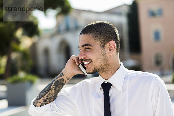 Lächelnder junger Geschäftsmann telefoniert mit Smartphone