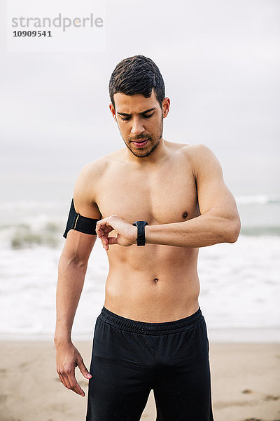 Sportlicher junger Mann am Strand mit Blick auf die Uhr