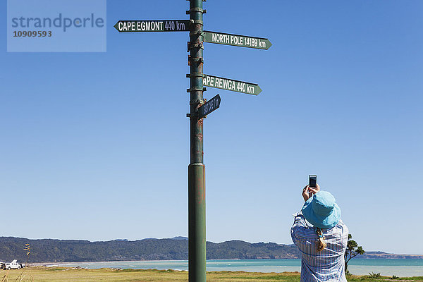 Neuseeland  Nordinsel  Ostkap  Frau macht Smartphone-Fotos von Wegweisern in Te Araroa