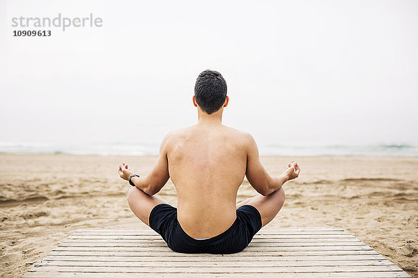 Junger Mann beim Yoga an der Strandpromenade