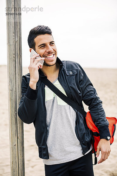 Lächelnder junger Mann am Handy am Strand