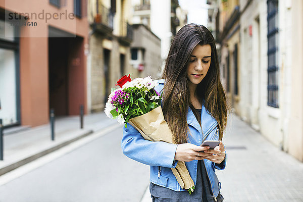Junge Frau mit Handy und Blumenstrauß in der Stadt