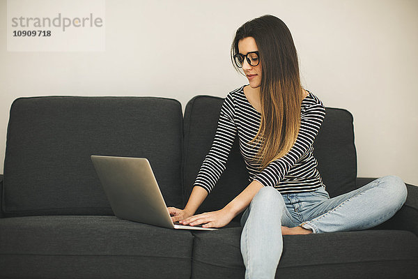 Junge Frau sitzt auf der Couch mit Laptop