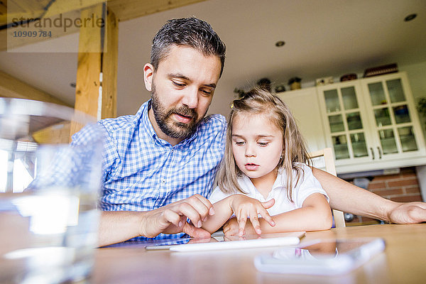 Vater und Tochter sitzen zu Hause mit digitalem Tablett