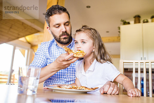 Vater füttert seine kleine Tochter mit Pizza.
