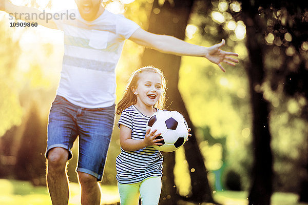 Glückliches kleines Mädchen mit Fußball  das mit seinem Vater im Park spielt.