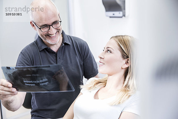 Zahnarzt  der dem Patienten ein Röntgenbild zeigt  auf dem Zahnarztstuhl sitzend