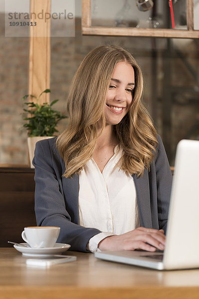 Porträt einer lächelnden jungen Frau mit Laptop im Coffee-Shop