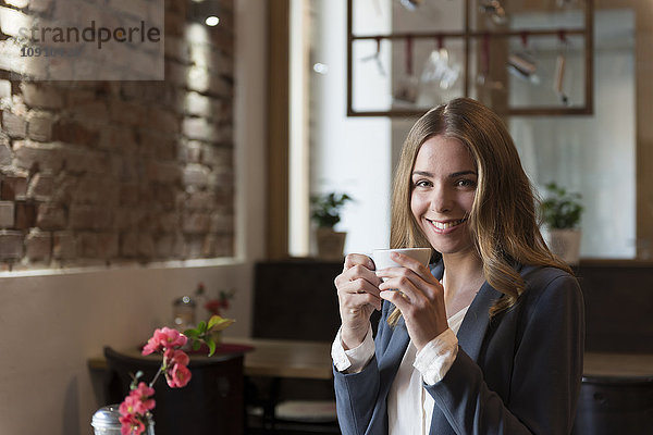 Porträt einer lächelnden jungen Frau beim Kaffeetrinken in einem Coffee Shop