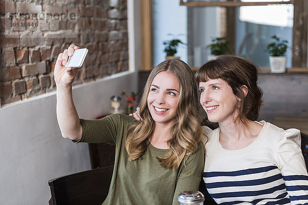 Zwei beste Freunde sitzen in einem Coffee-Shop und nehmen Selfie mit Smartphone.