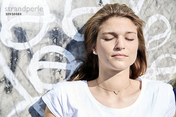 Porträt einer jungen Frau mit geschlossenen Augen vor einer Wand