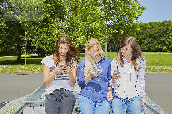 Drei Freunde sitzen Seite an Seite mit ihren Smartphones