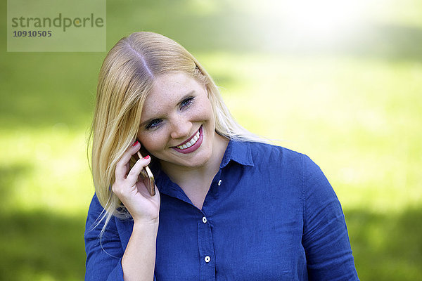 Lächelnde junge Frau telefoniert mit Smartphone im Park