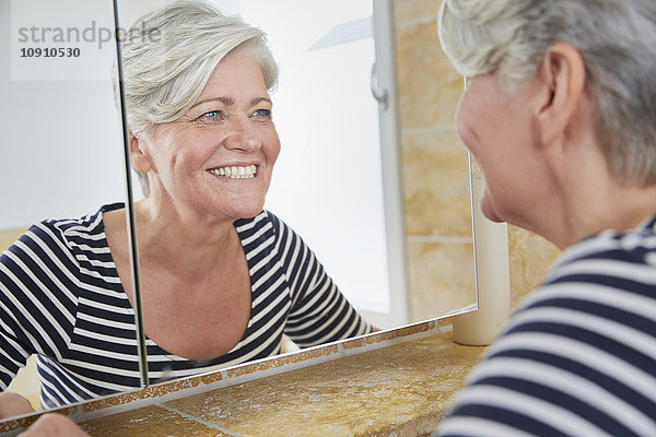 Porträt einer lächelnden Frau  die sich im Badezimmerspiegel sieht.