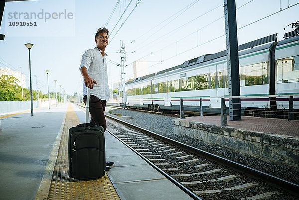 Junger Mann mit Koffer wartet am Bahnsteig.