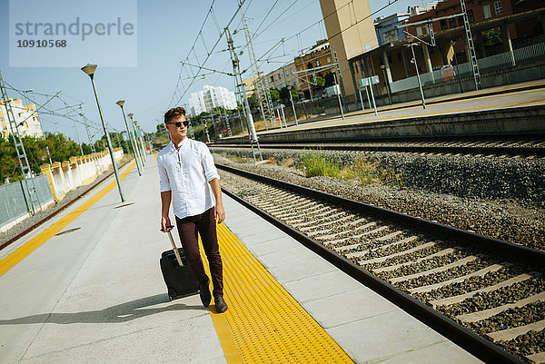 Junger Mann mit Koffer auf dem Bahnsteig