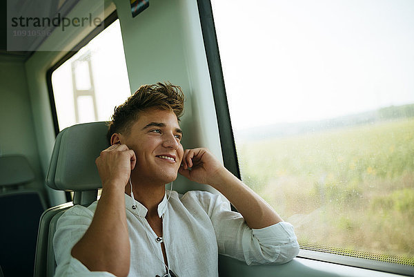 Junger Mann hört Musik und lächelt im Zug