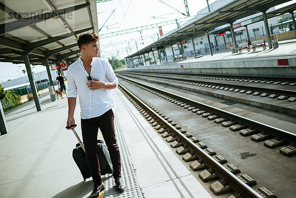 Junger Mann mit Koffer wartet am Bahnsteig.