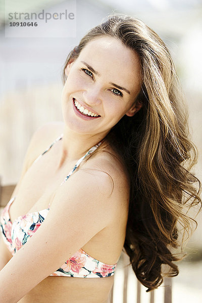 Porträt einer lächelnden jungen Frau mit langen braunen Haaren im Bikini-Top