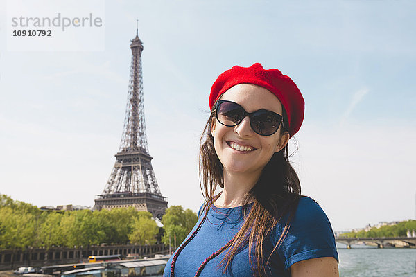 Frankreich  Paris  Porträt einer lächelnden Frau mit Sonnenbrille und roter Baskenmütze vor dem Eiffelturm