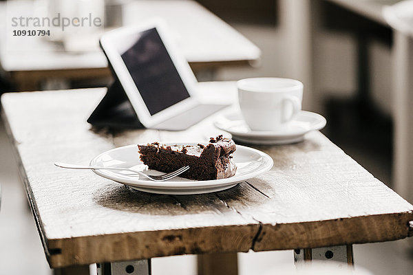 Kuchenstück auf dem Tisch in einem Café mit Tasse Kaffee und digitalem Tablett